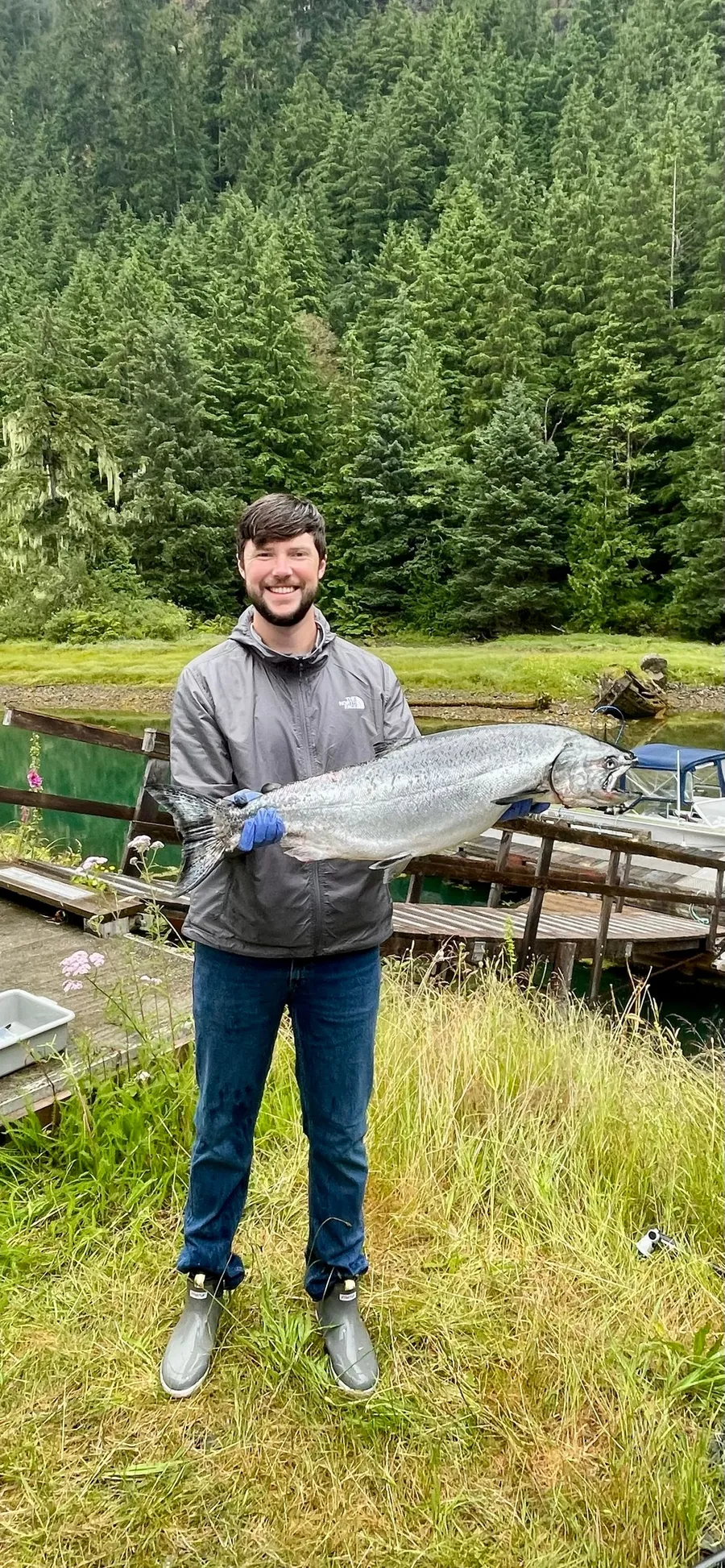 Parker holding a large salmon on a dock in front of an evergreen forest.
